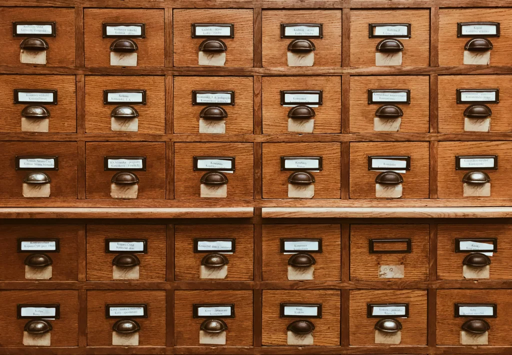 The image shows a wooden card catalog with multiple drawers, each fitted with a metal handle and a small labeled tag. The labels are in Czech, with various inscriptions like "Kolektiv," "Koncepce," "KS Názevka," and others. This traditional card catalog system is used for organizing and accessing information. This image is featured in an article with the theme "use internal data with AI".